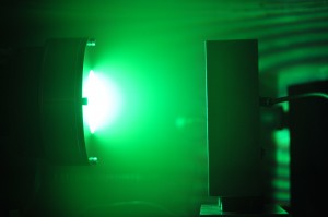 In this photograph of Berkeley Lab’s system for “self-sputtering far above the runaway threshold,” neutral excited copper atoms in the plasma glow green while, near the magnetron target, a plentiful supply of ions glows white.