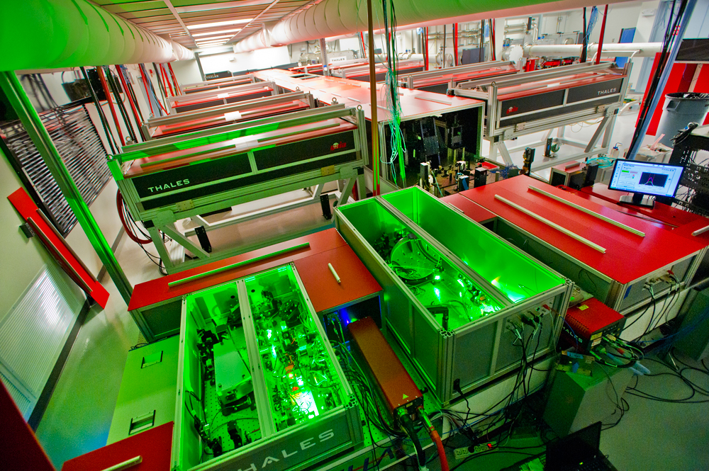 The BELLA laser under construction. In the foreground, units of the front end stretch and amplify short, relatively weak laser pulses before further amplification in the long central chamber. Amplification is done by titanium sapphire crystals boosted by a dozen pump lasers. At the far end of the hall the now highly energetic stretched pulse is compressed before being directed to BELLA’s electron-beam accelerator component. (Photo Roy Kaltschmidt, Lawrence Berkeley National Laboratory) 
