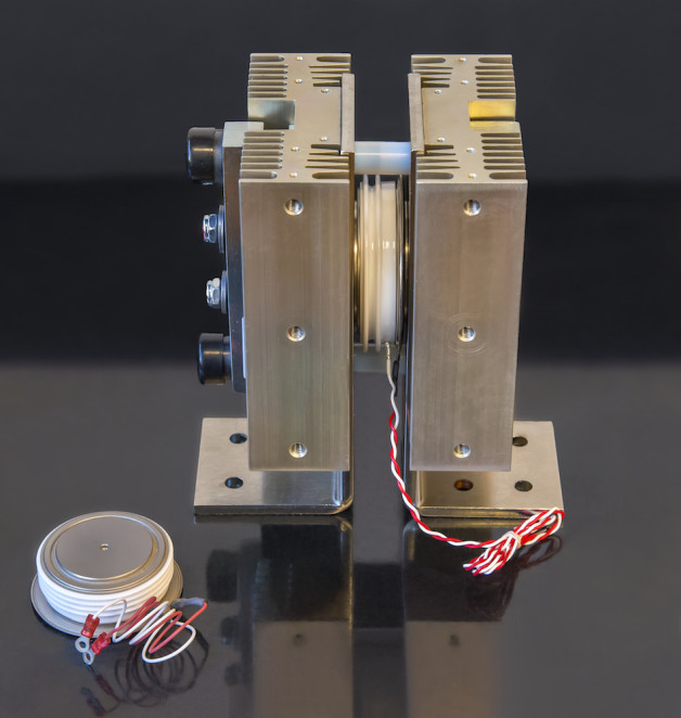 Photo - Examples of thyristor types that have been used at Berkeley Lab: the palm-sized thyristor at bottom left is an example of a typical device, with red and white trigger wires. On the right, a thyristor (middle) is mounted between two metal heatsinks, which conduct heat away and help cool the device during high-power operation. (Roy Kaltschmidt/Berkeley Lab)