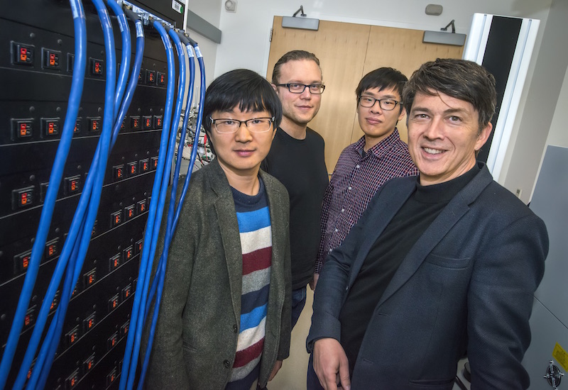 Four researchers standing next to a supercomputer.