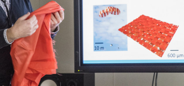 Photo - Francesco Panerai holds a sample of spacecraft parachute material at NASA Ames Research Center. The screen display shows a parachute prototype at left and a small patch of the material at right. (Credit: Marilyn Chung/Berkeley Lab)