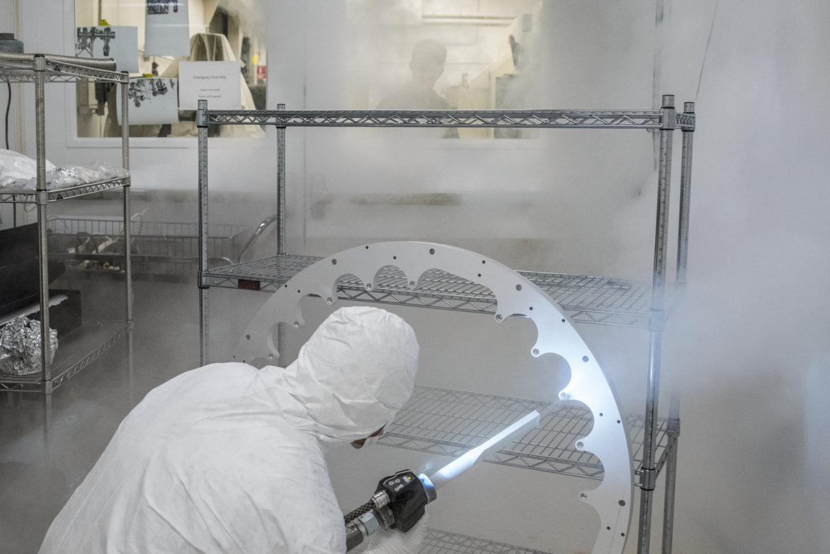 Photo - Mechanical Engineer Joe Wallig prepares a metal ring component of the injector gun for installation using a jet of high-purity dry ice in a clean room. (Credit: Marilyn Chung/Berkeley Lab)