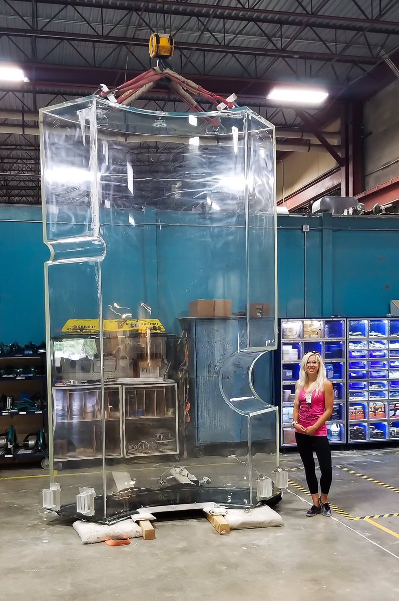 Photo - Sally Shaw, a UC Santa Barbara postdoctoral researcher, stands beside a 12-foot-tall acrylic tank at a manufacturing site in Colorado. The tank was built for the LUX-ZEPLIN dark matter search experiment now under construction in Lead, South Dakota. (Credit: LZ Collaboration)