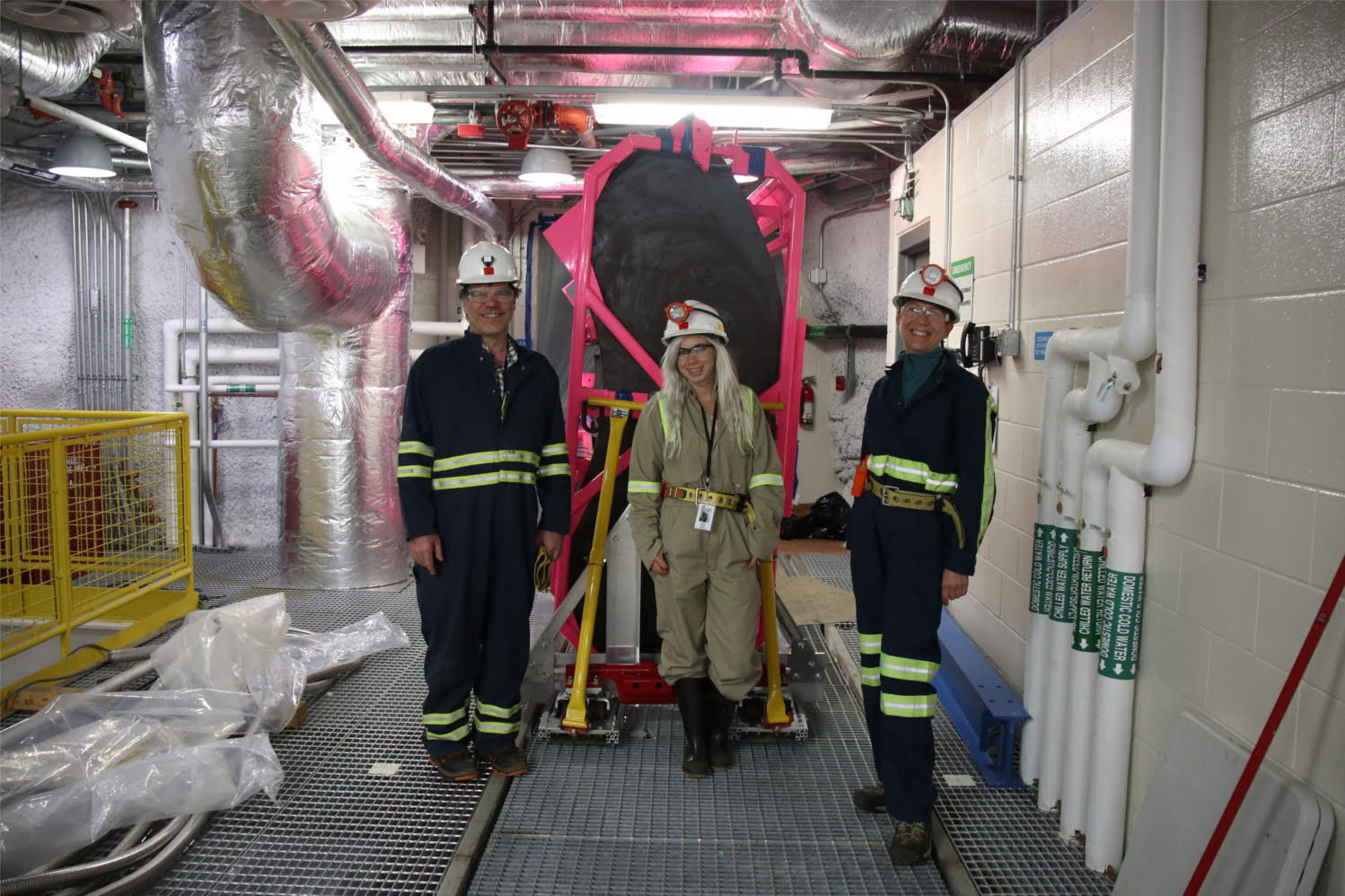 Photo - From left to right: LZ Chief Engineer Jeff Cherwinka, UC Santa Barbara postdoctoral researcher Sally Shaw, and UC Santa Barbara engineer Suzanne Kyre in teh Sanford Underground Research Facility's Davis Laboratory on Oct. 11. Behind them is a support frame, custom cart, and steel tank mockup that was tested for the delivery of acrylic tanks. (Credit: Constance Walter/Sanford Underground Research Facility)