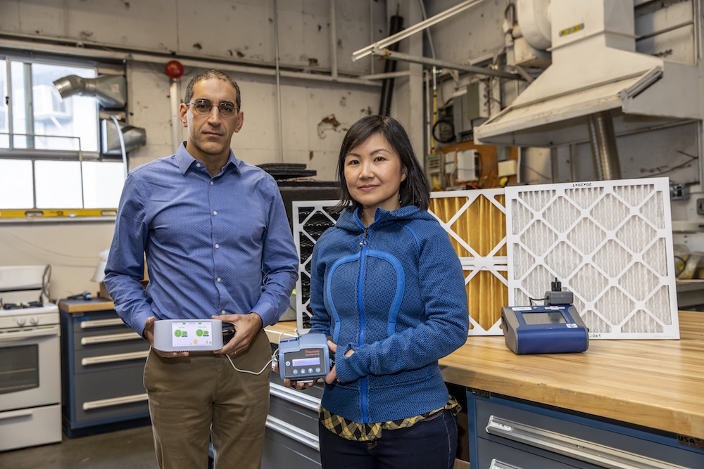 Two scientists pose together holding sensors used to measure indoor air quality.