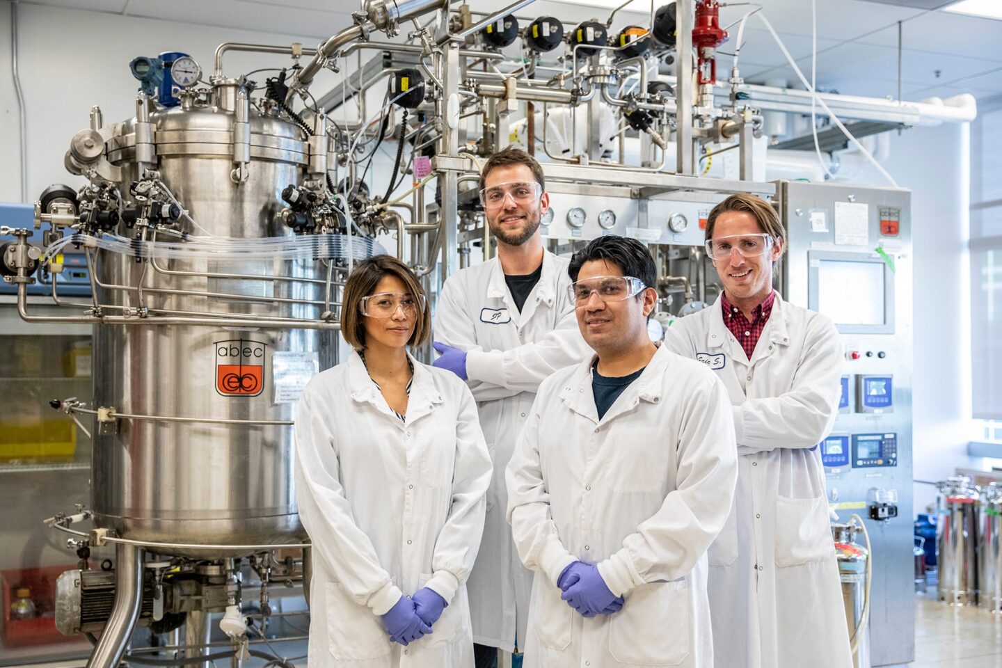 Nina Reyes (left) and Dino Athanasiadis (front center) of Checkerspot and Jan-Philip Prahl (back center) and Eric Sundstrom (back right) stand in front of a bioreactor at the ABPDU during optimization testing of their fermentation process.