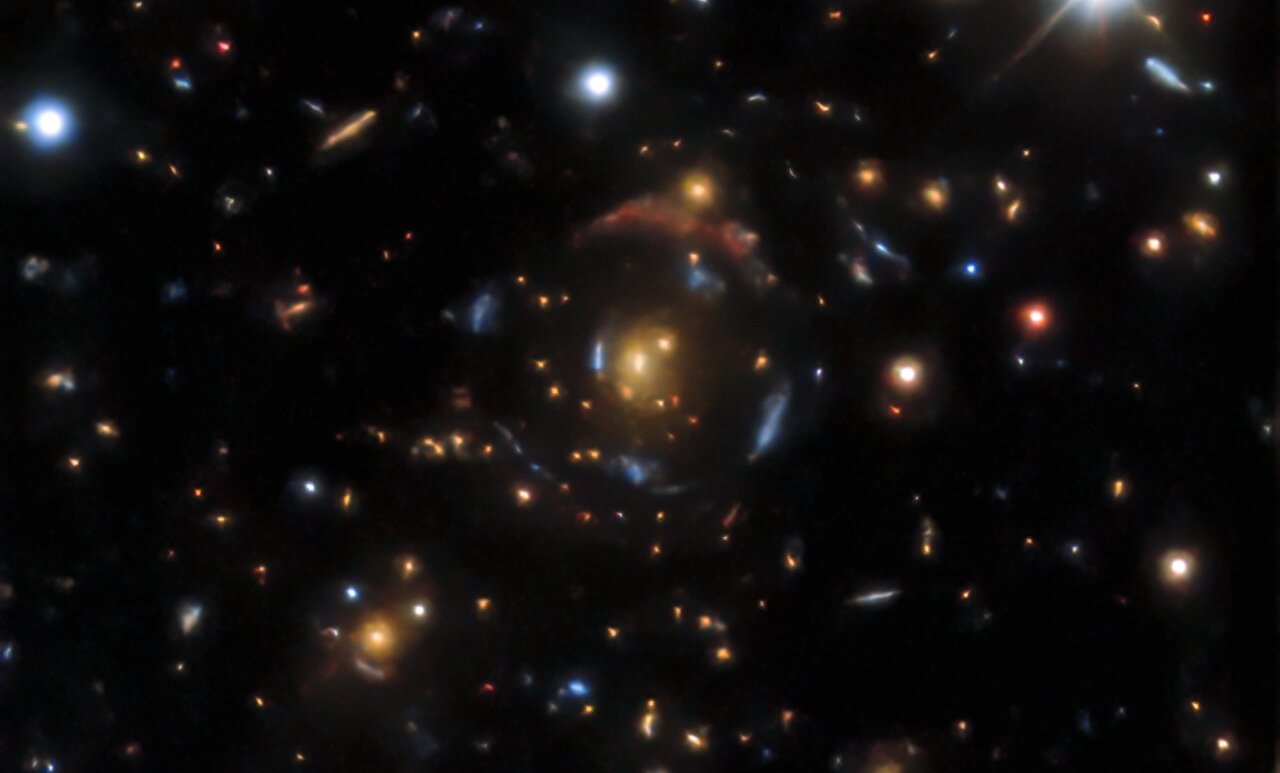 Image - A gravitational lens found in the DESI Legacy Surveys data. There are four sets of lensed images that correspond to four background galaxies, which appear as partial rings around an orange galaxy at the center and foreground. (Credit: DESI Legacy Imaging Surveys, Berkeley Lab, DOE, KPNO, CTIO, NOIRLab, NSF, AURA)