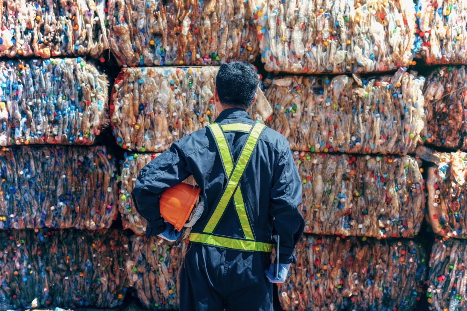 Person holding an orange hardhat and standing in front of bricks of plastic.