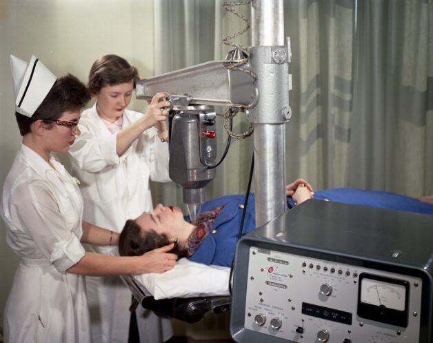Historical photo of two health care workers working an X-ray machine.