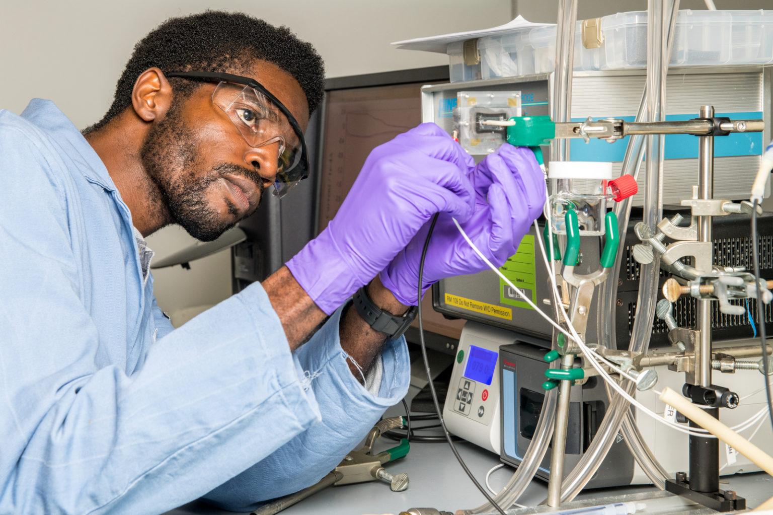 A scientist wearing gloves handles lab equipment.