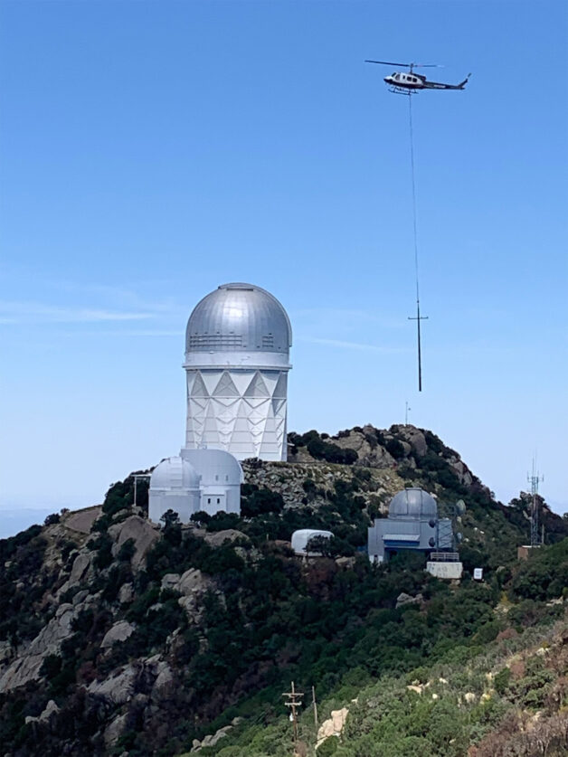 Telescope on top of a mountain with a helicopter carrying a power pole nearby.