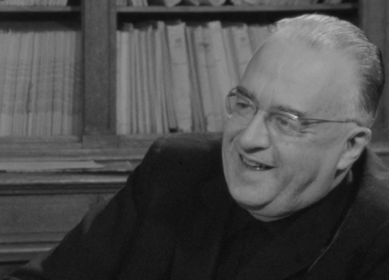 Still frame from a black and white video that shows Georges Lemaître, a man with short hair and glasses, at the end of the interview.