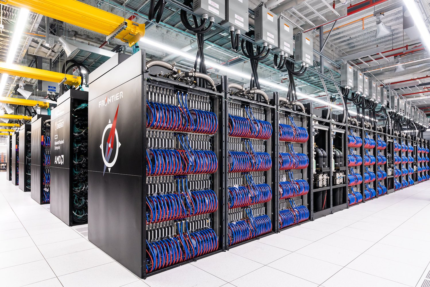 A large white room filled with rows of tall black containers holding computer components with blue and red wiring visible