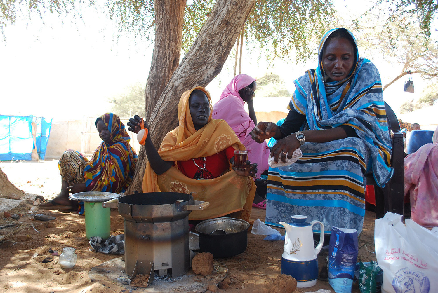 Women in traditional clothing sitting and making tea outdoors with the Berkeley-Darfur Stove.