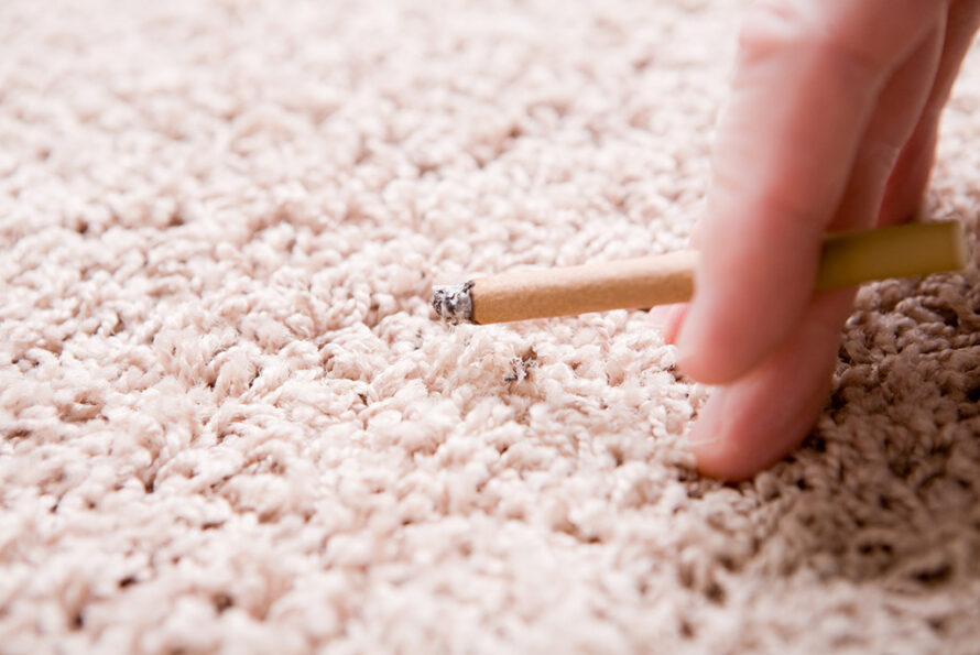Hand holding a cigarette near carpet.