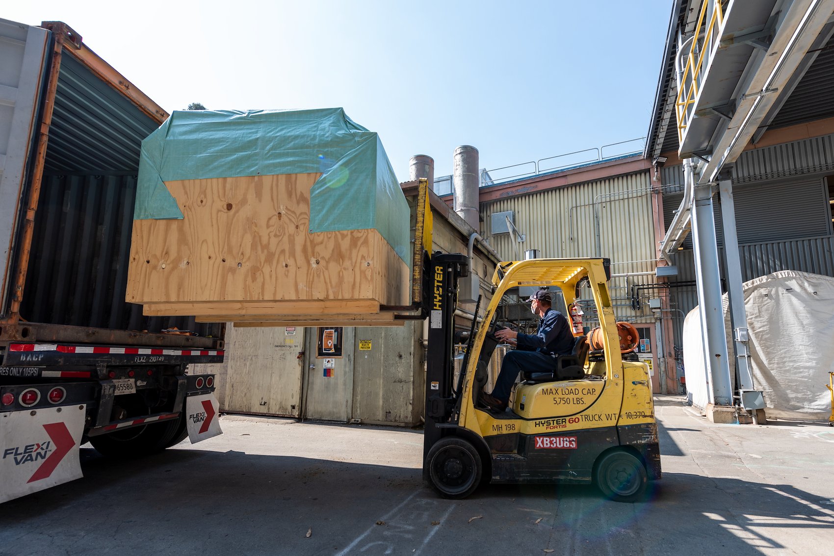 A forklift pulls a large plywood box out of a truck