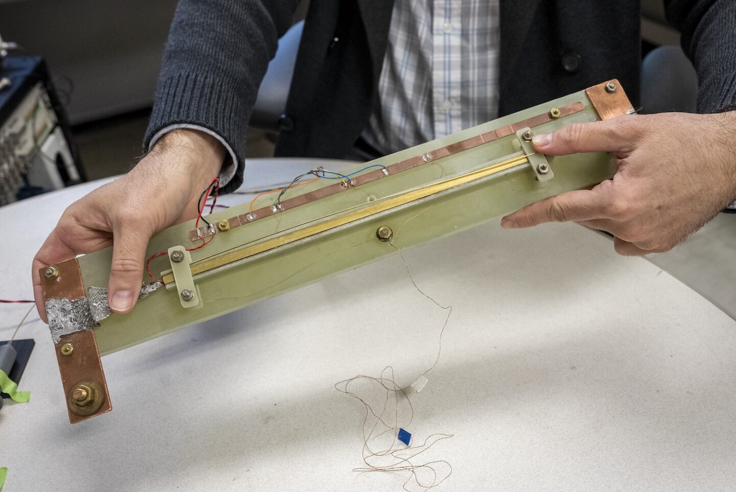 A long thin board approximately 3 by 14 inches with a strip of superconducting material and a heating wire above it.