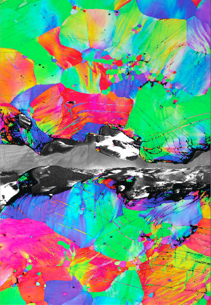 A field of pink, purple, cyan, indigo, orange, and yellow shapes packed together, resembling vibrant abstract art. A black and white crack cuts across the center of the frame.