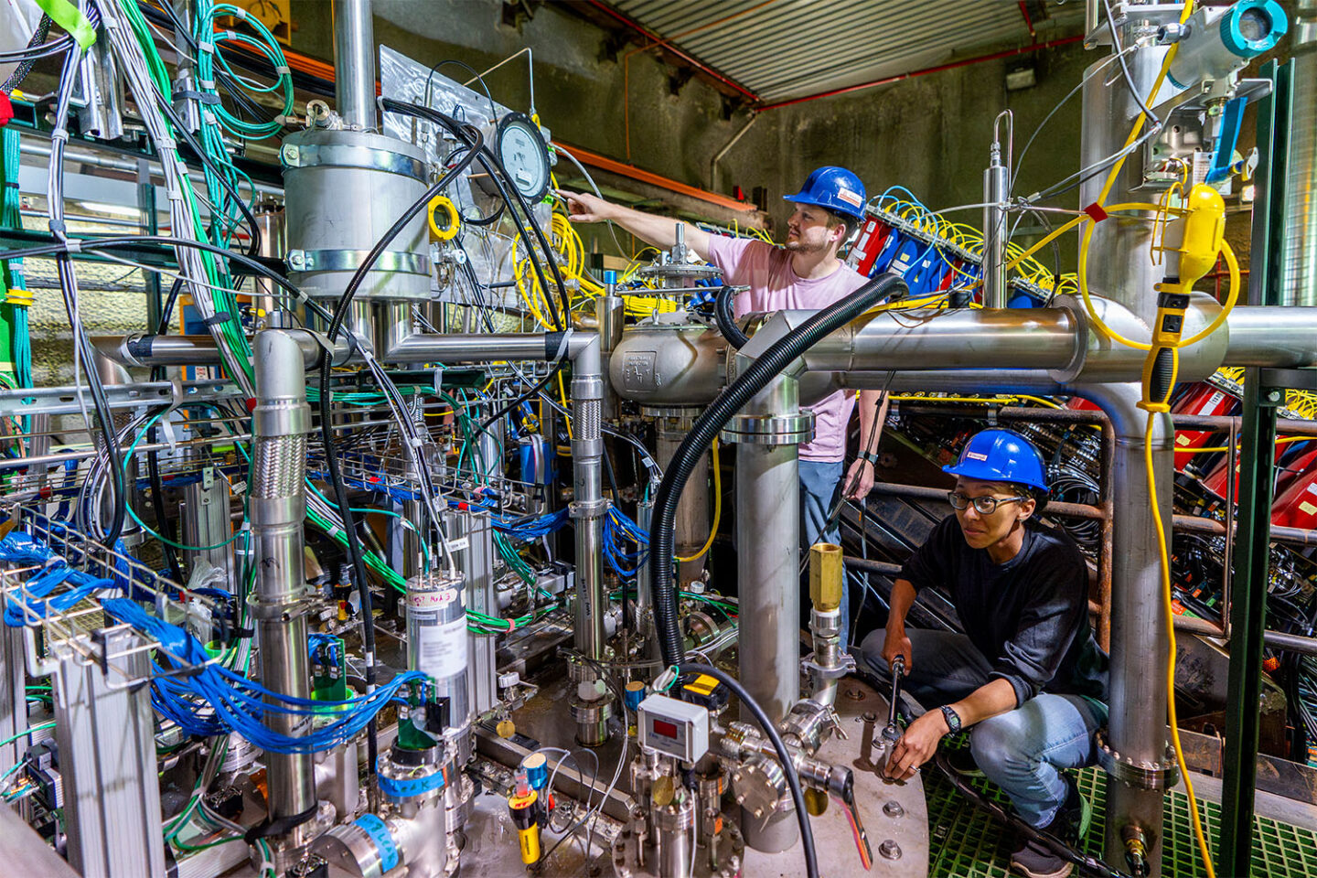 Two scientists in hard hats working on the 2x2 prototype detector for the DUNE near detector.