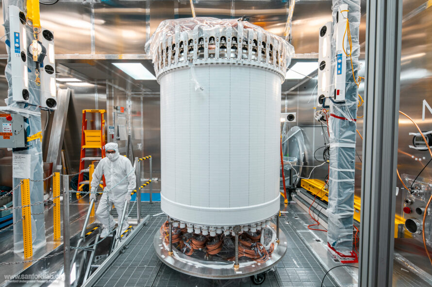 A person in protective gear descending the stairs next to LZ's central detector, the time projection chamber, in a surface lab clean room before delivery underground.