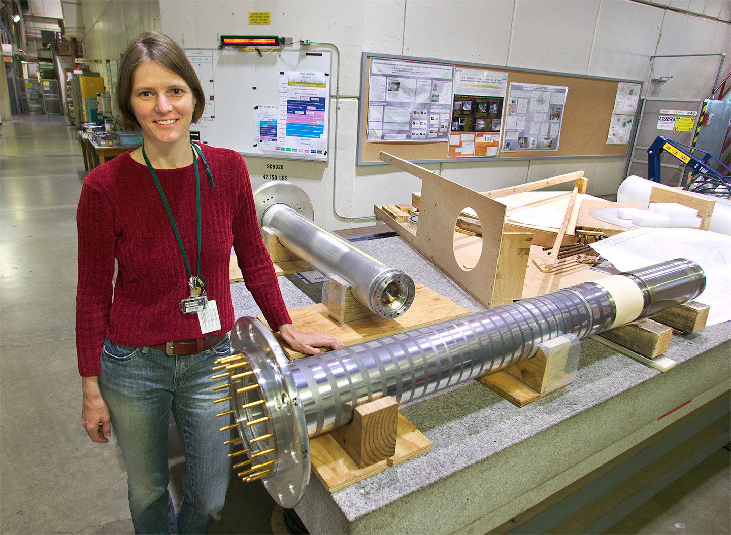 A person wearing a red top and jeans standing next to the 88-inch Cyclotron's VENUS ECR ion source plasma tube in the Lab.