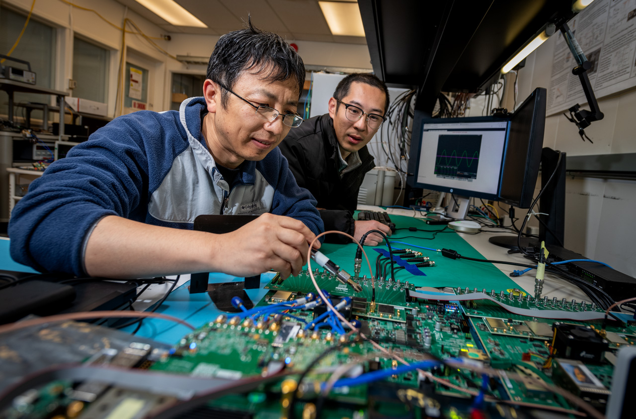 Two researchers examining electronic components and computer boards in a lab setting.