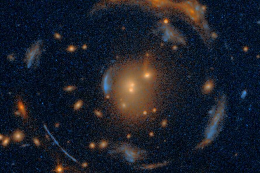 The Carousel Lens, an alignment consisting of 1 foreground galaxy cluster (the ‘lens’) and 7 background galaxies spanning immense cosmic distances through the gravitationally distorted space-time around the lens, as seen through the Hubble Space Telescope.