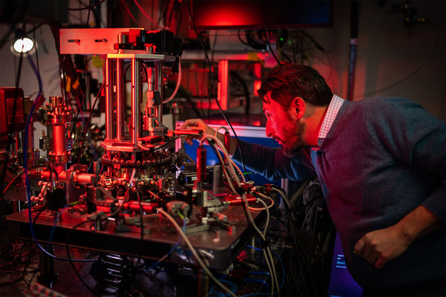 Technical staff member works on trapped-ion systems in a dark lab illuminated by red lights.