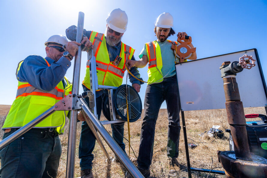 Three people wearing hard hats and safety gear setting up sensors.