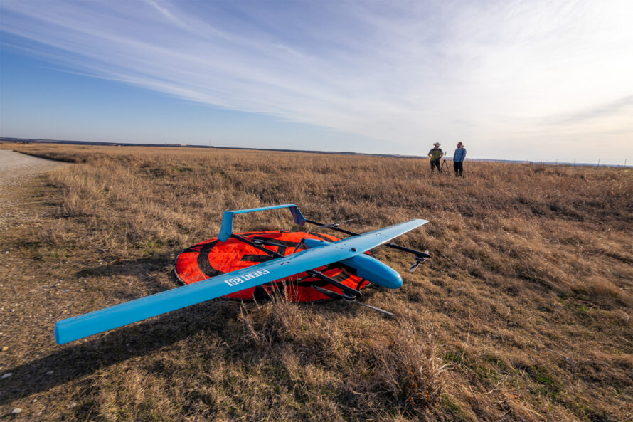 A drone lying in a field, with two people in the background.