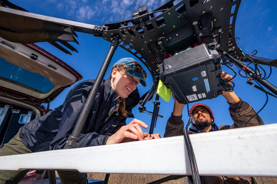 Two people preparing a drone for field surveys outdoors.