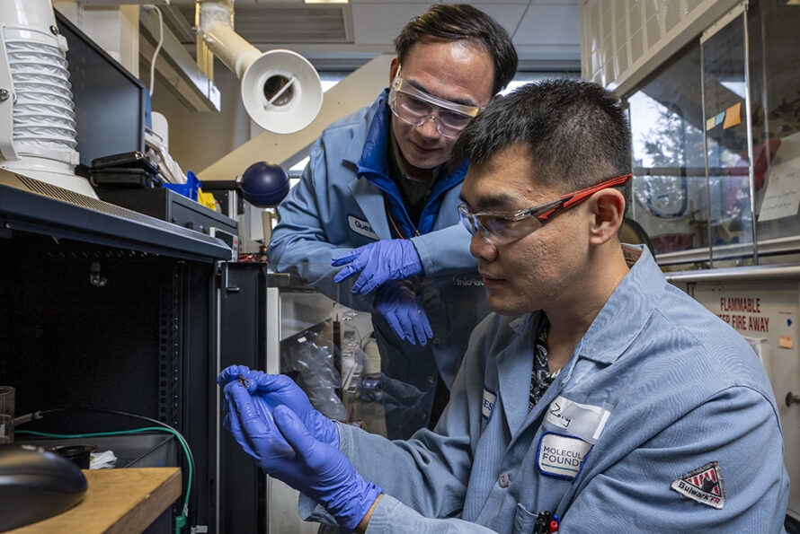 Two researchers in blue coats and safety glasses look at an experimental setup.