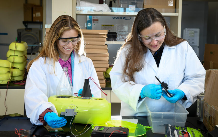 Two smiling researchers in white lab coats working at a lab bench.