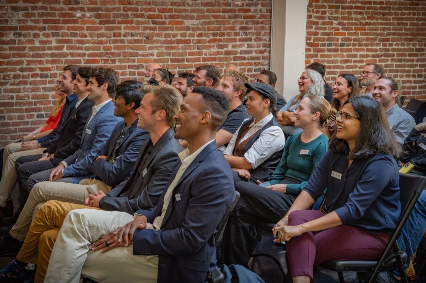 A large audience sitting and watching a speaker toward the left.