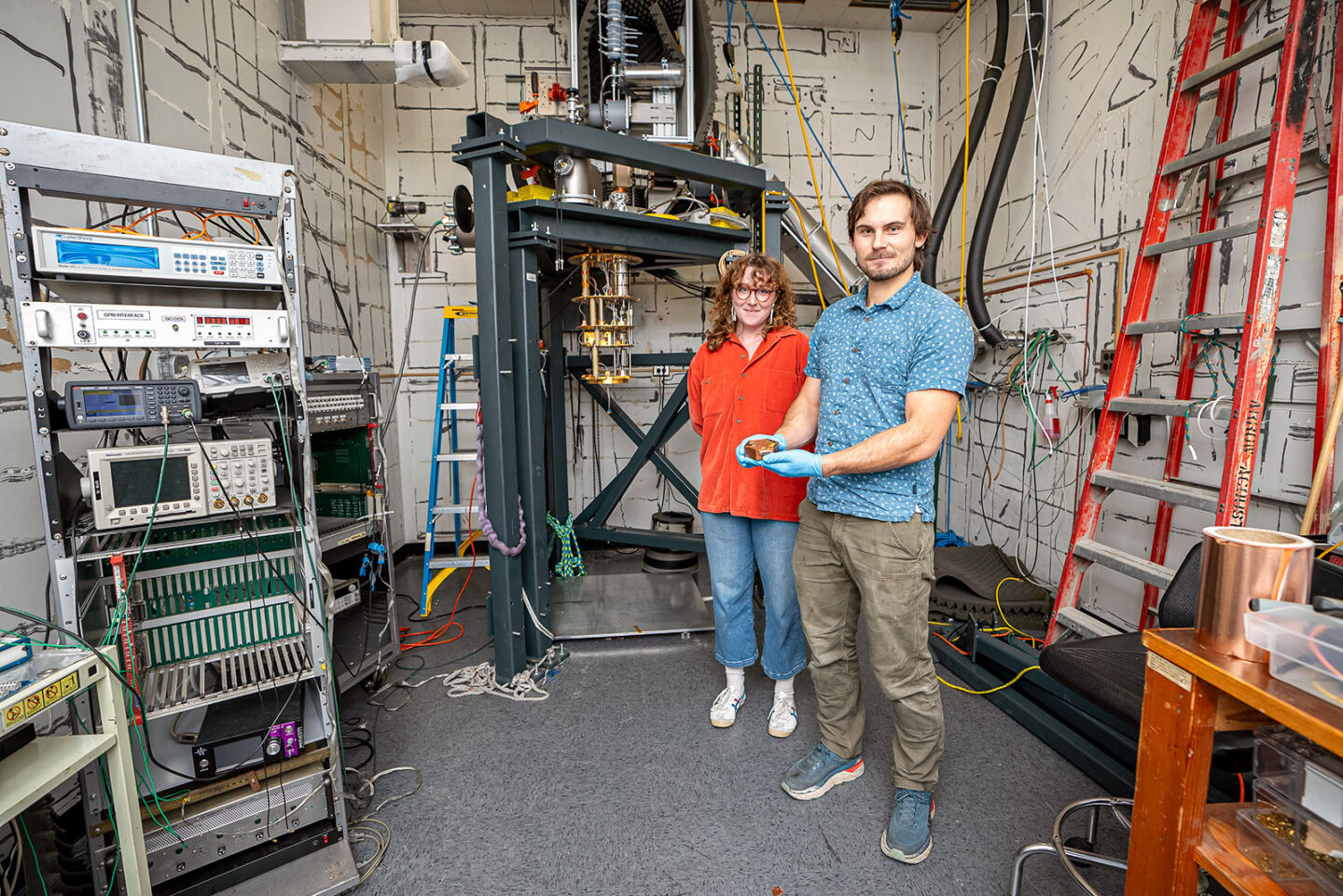 Two researchers stand in a laboratory, with one holding the TESSERACT detector with gloved hands.