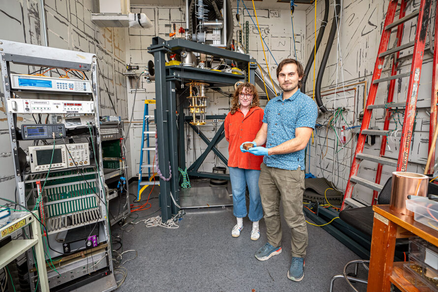 Two researchers stand in a laboratory, with one holding the TESSERACT detector with gloved hands.