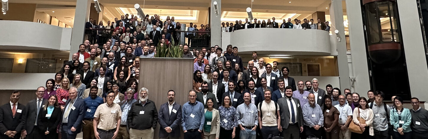 Group of attendees gathered for a group photo across multiple levels of a lobby with a central staircase.