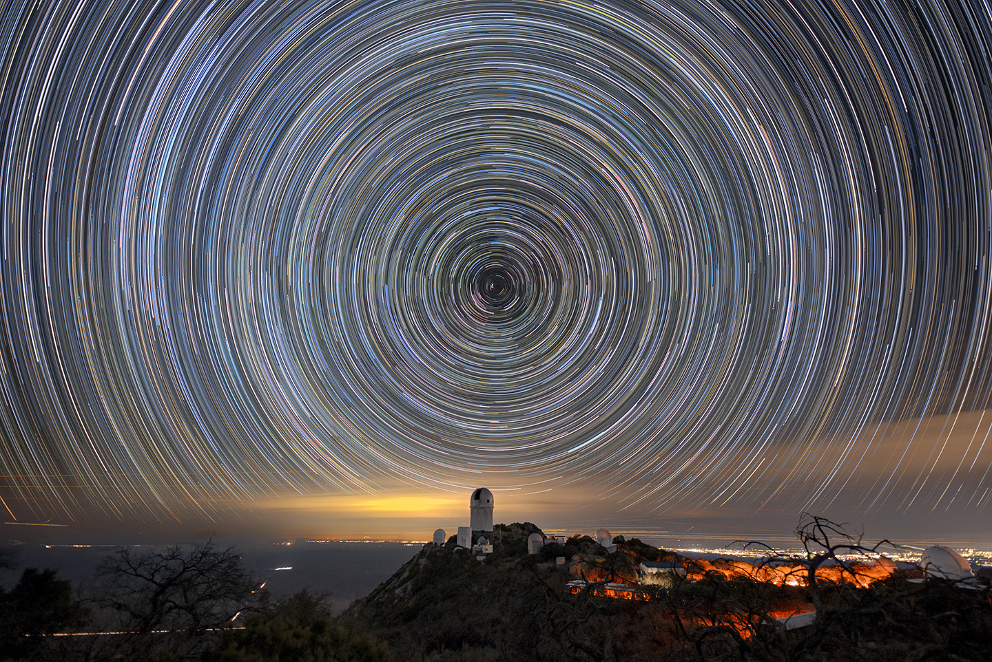 Circles of light on the night sky. A telescope dome atop a mountain is below the center of the circle.