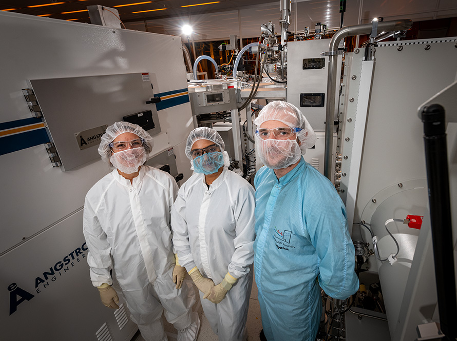 Three scientists dressed in protective clothing stand in a bright laboratory.