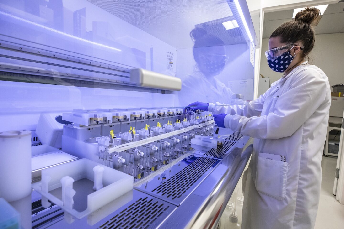 A researcher in a Lab coat and face mask operates a machine at the Lab.