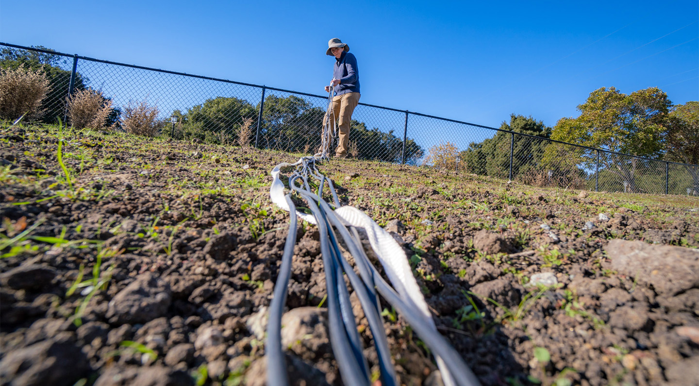 Woman on a slope holding fiber cables that extend downhill.