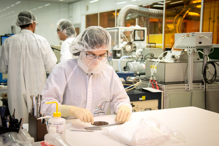 A clean room with employees working at workstations on the left, a work table in the center with an employee looking down at a sample.