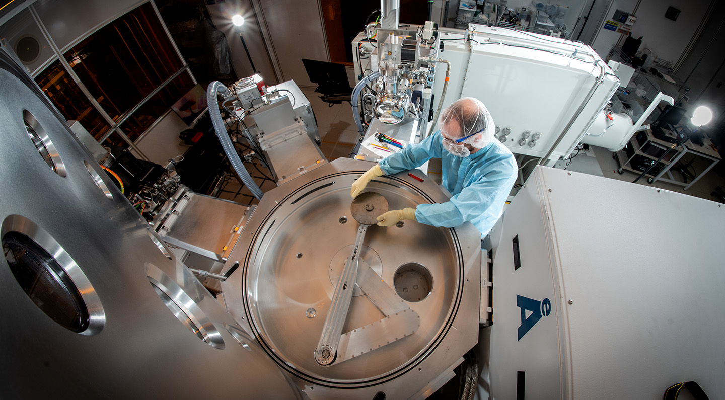 A person in protective gear works on a large piece of scientific equipment.