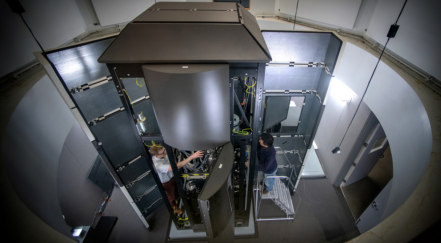Two people work on a large microscope