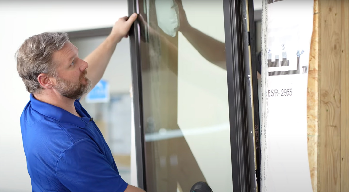 A person in a blue shirt installing a large glass panel into a frame.