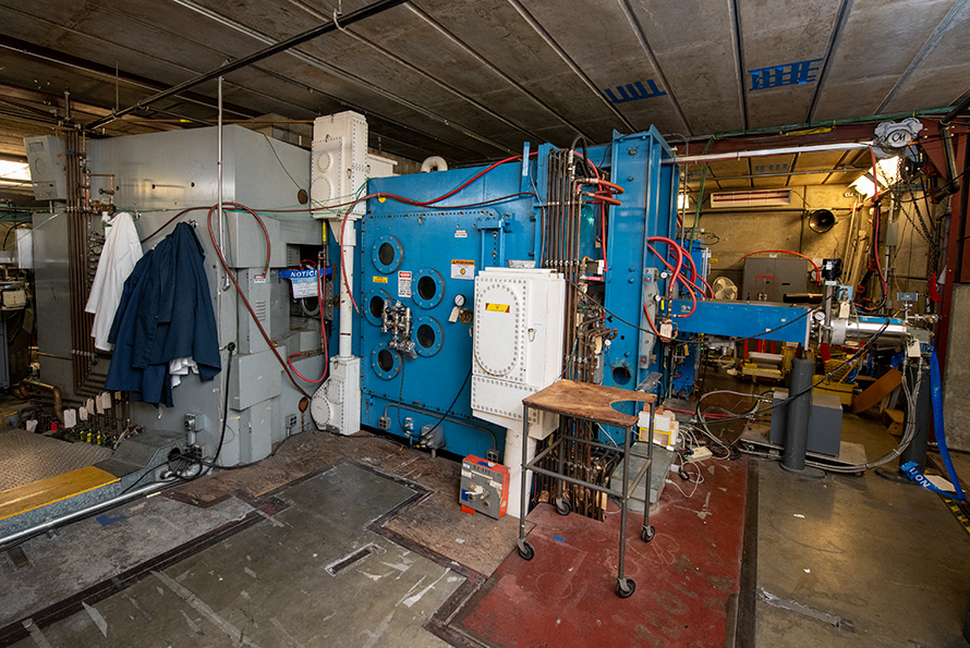 A scientific laboratory with various wires and machinery. A grey 88-inch cyclotron is in the left corner and a blue radiofrequency tank is to the right.