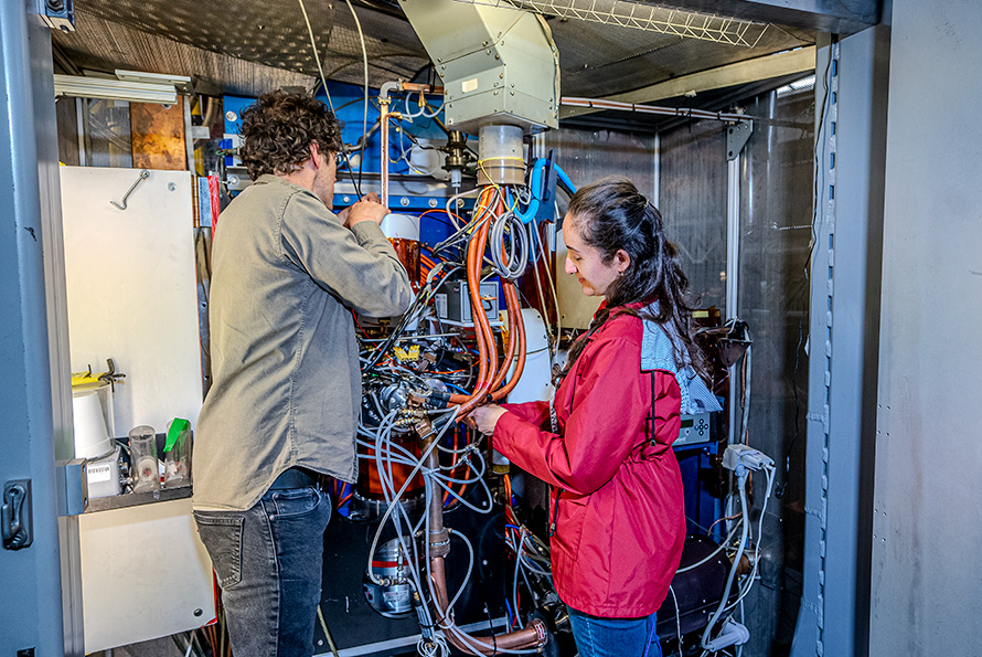 Two researchers make adjustments to an experimental setup that is covered with multicolored wires.