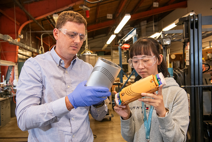 Two researchers in protective gear handle grey and yellow prototypes of elliptical-aperture CCT magnets.