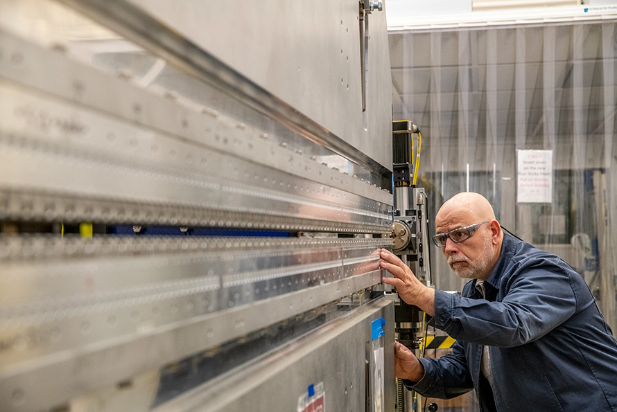 A researcher in protective glasses inspects a large, wall-like metal undulator.