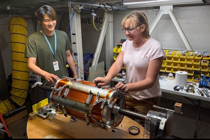 Two researchers in a laboratory space adjust a device that sits on a circular table